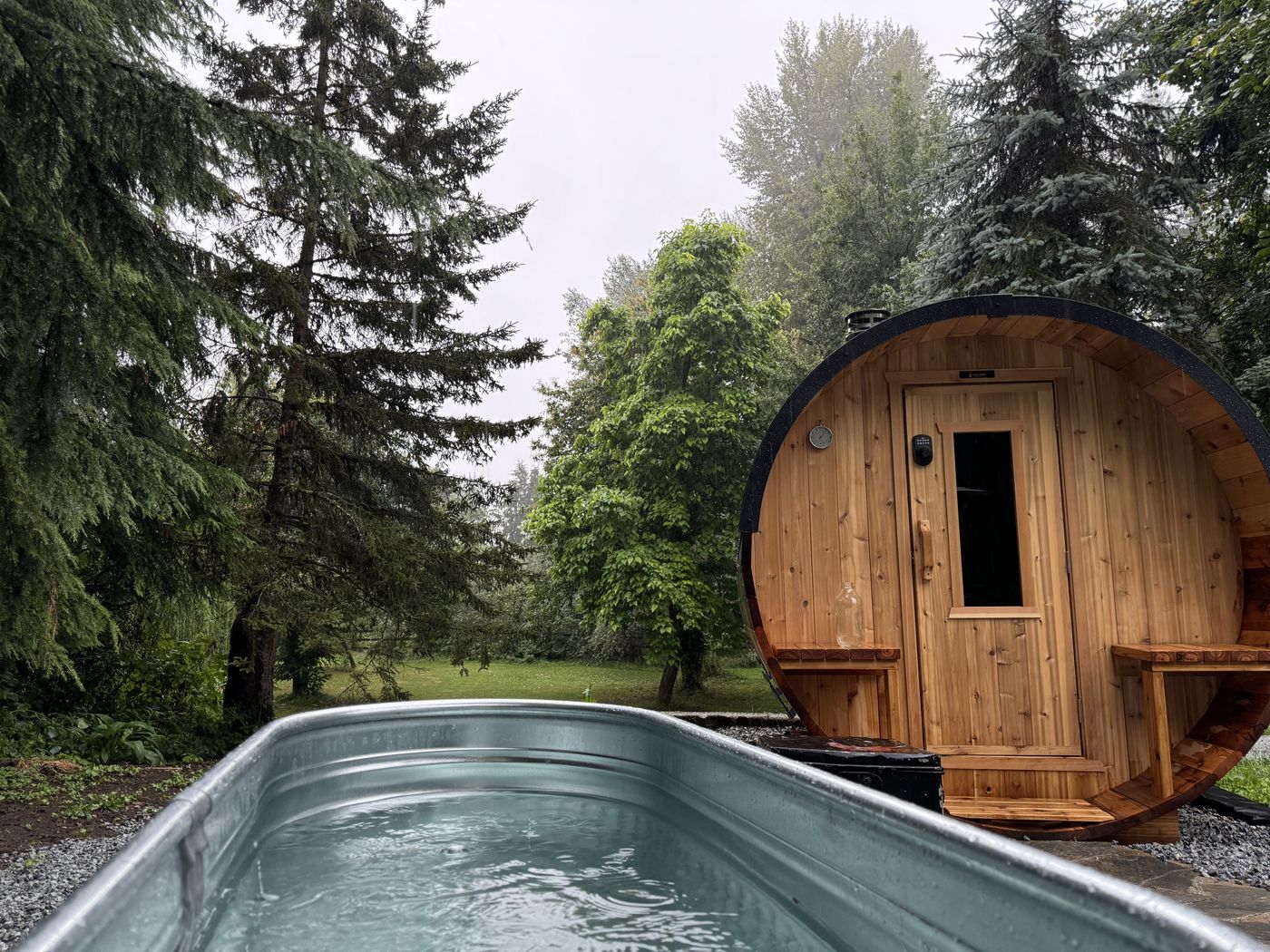 Cedar barrel sauna beside a cold plunge pool in a forest setting